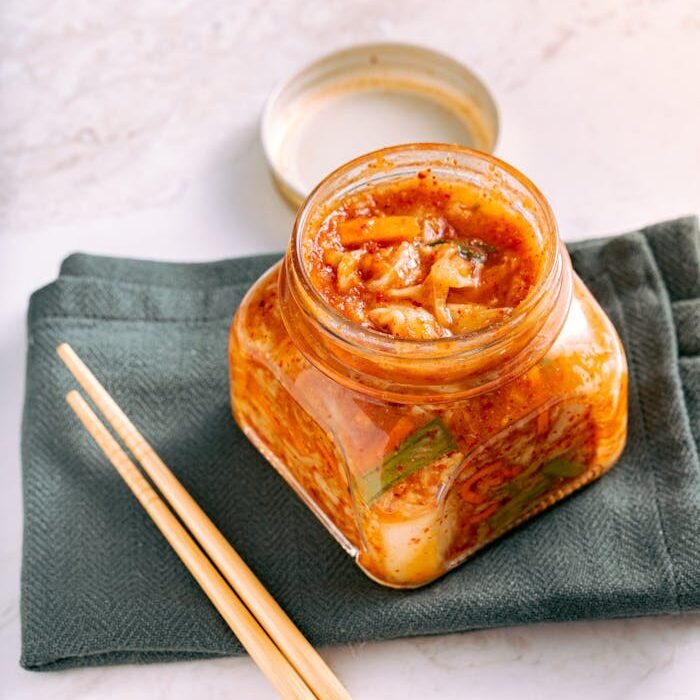 A jar of traditional homemade kimchi on a marble surface with wooden chopsticks beside it.