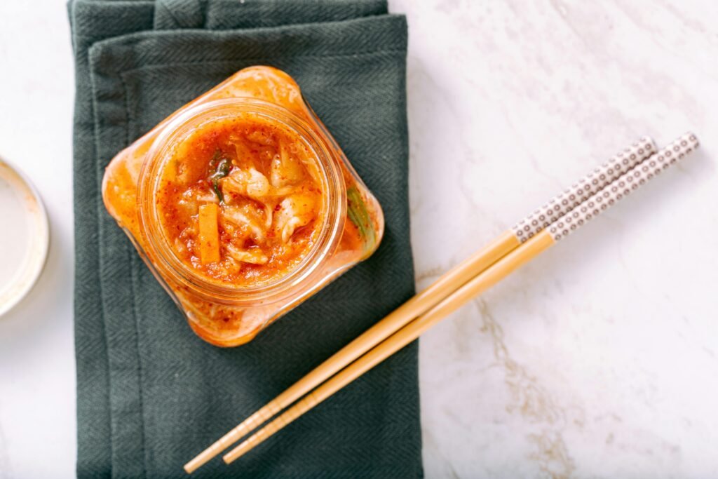 pexels-photo-6823262-6823262-1 Delicious homemade kimchi in a glass jar with wooden chopsticks on a green napkin.