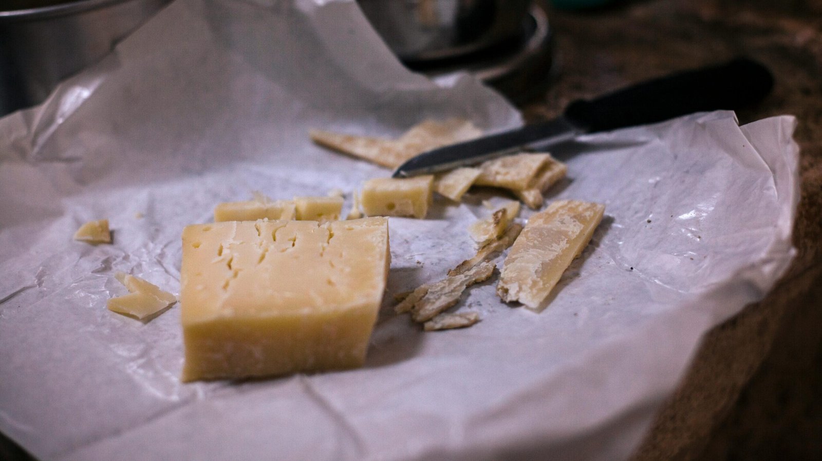 A block of cheese with slices and a knife on rustic paper, showcasing a natural and artisanal feel.