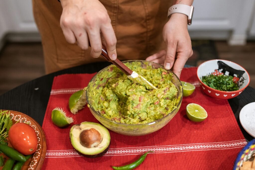 Close-up of hands mixing homemade guacamole with fresh ingredients in a kitchen setting.
